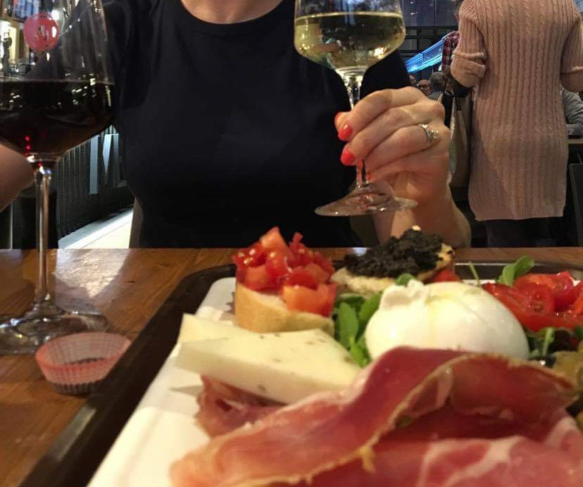 A semi-blurred but authentic image of the editor with another person, cheers-ing over a plate of antipasto.